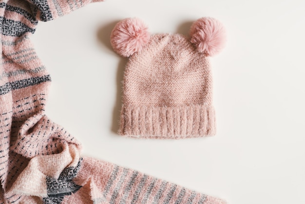 Bonnet tricoté à la main avec deux pompons et écharpe chaude de couleur rose sur fond blanc, vue de dessus. Vêtements d'automne et d'hiver