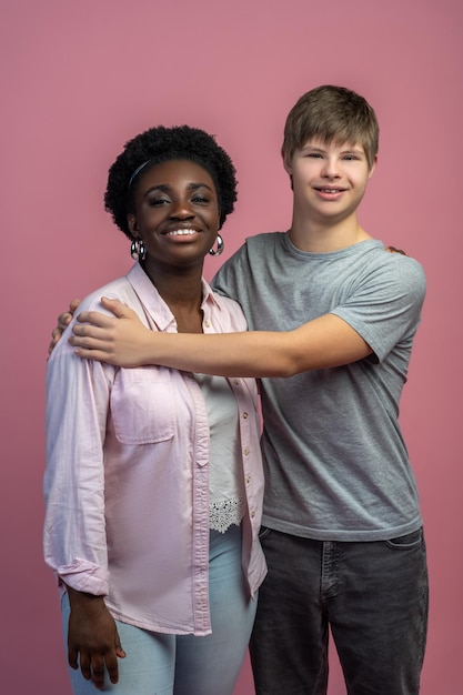 Bons moments. Heureux homme caucasien avec le syndrome du duvet étreignant une femme afro-américaine regardant la caméra debout sur fond clair