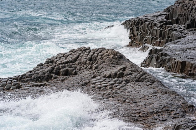 Bord de mer rocheux formé par des colonnes de basalte contre le paysage côtier de la mer orageuse des îles Kouriles