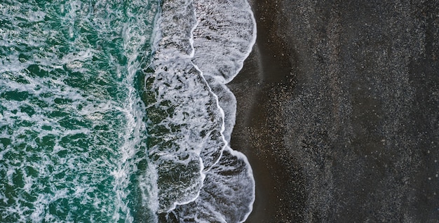Bord de mer avec une texture dramatique de vagues déferlantes et de sable noir, perspective de drone