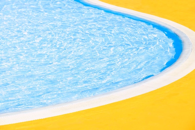 Le bord de la piscine extérieure avec une bordure incurvée dans une journée d'été ensoleillée Eau bleue claire et sol jaune