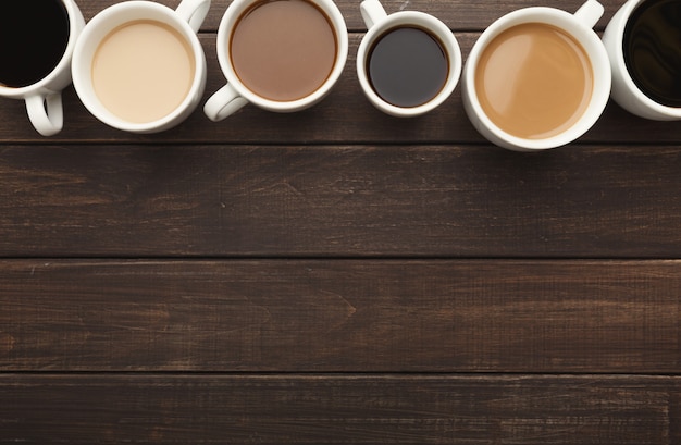 Bordure de divers types de café dans des tasses de différentes tailles sur une table en bois rustique, vue de dessus, espace pour copie