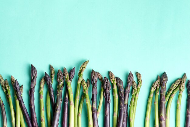 Bordure de légumes à partir de lances d'asperges crues naturelles fraîches pour la cuisson des aliments diététiques faits maison sur fond bleu.