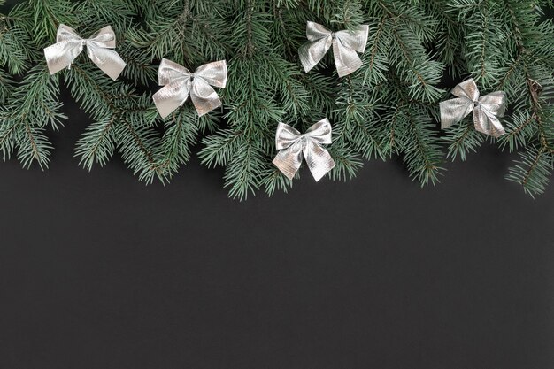 Bordure de Noël avec des branches de sapin et des arcs argentés sur fond noir.