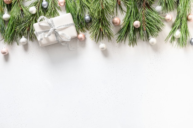 Bordure de Noël avec cadeau blanc, boules pastel rose et argent, branches à feuilles persistantes sur blanc. Vue de dessus. Mise à plat