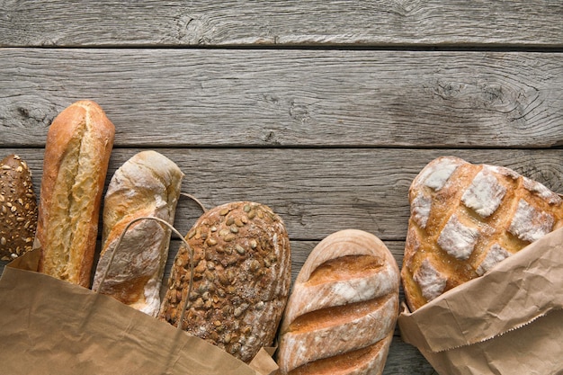 Bordure de pain sur bois rustique avec fond d'espace de copie. Composition de nature morte de pains à grains entiers bruns et blancs avec de la farine de blé saupoudrée autour.