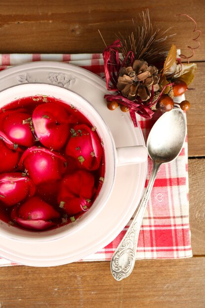 Bortsch rouge clair polonais traditionnel avec des boulettes dans un bol sur un plateau et sur une table en bois