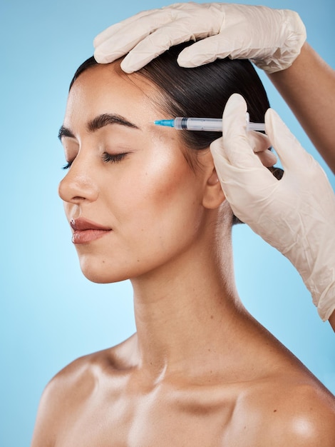 Botox de soins de la peau et femme dans un studio avec une esthéticienne pour le traitement de chirurgie esthétique et plastique de remplissage du visage Cosmétologie de beauté et modèle féminin recevant une injection faciale sur fond bleu