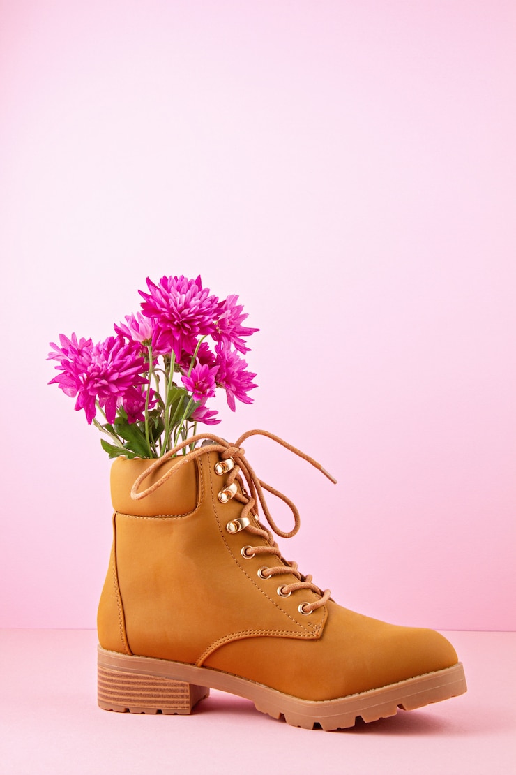 Photo bottes de randonnée avec des fleurs roses à l'intérieur sur le fond pastel rose.