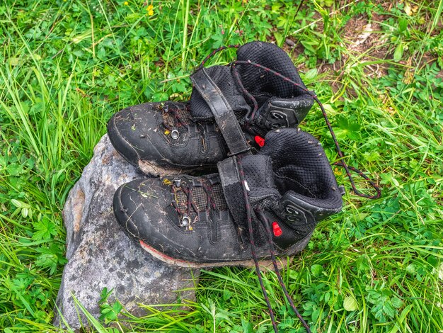 Des bottes de randonnée noires humides sèchent sur une pierre sur fond d'herbe verte. Difficultés de la randonnée, séchage des vêtements dans la nature.