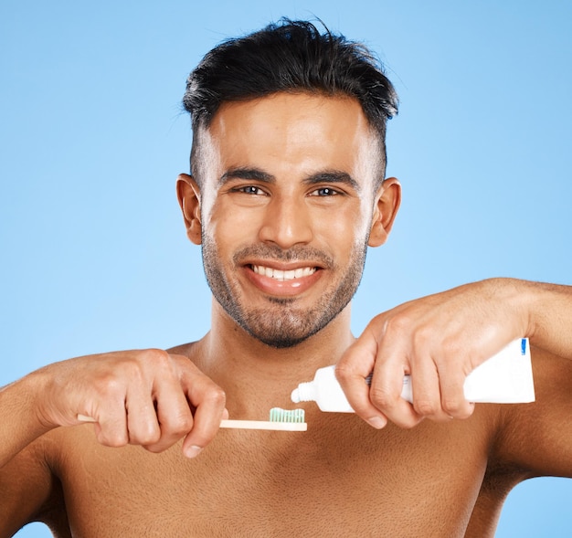 Bouche dentaire et homme se brosser les dents en studio pour le bien-être, la santé et le toilettage sur fond bleu Portrait visage et dents d'un indien heureux avec un dentifrice et une maquette de produit de nettoyage oral