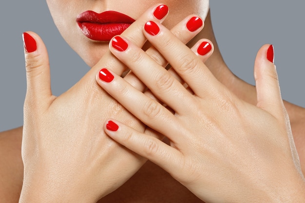 Photo bouche et ongles féminins avec manucure rouge et rouge à lèvres.