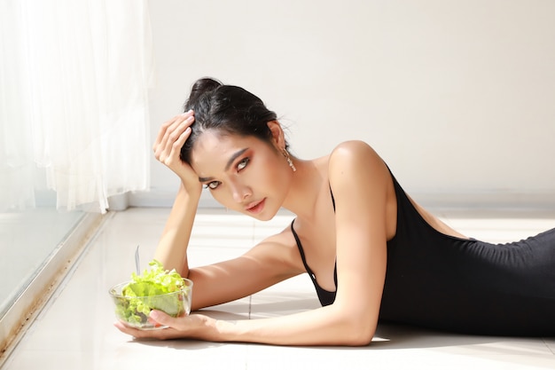 Bouchent belle jeune femme asiatique saine et sportive tenant le bol de salade et manger après la formation