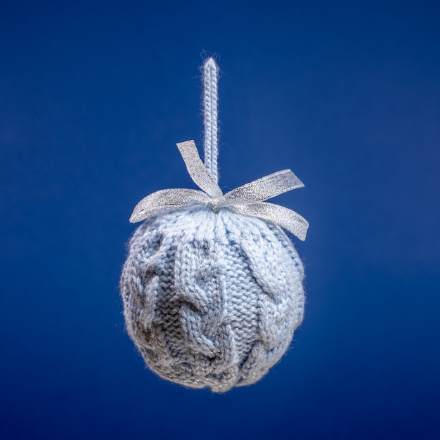 Bouchent une boule de Noël créative tricotée grise suspendue sur un carré bleu vif