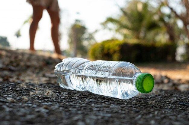 Bouchent la bouteille d'eau en plastique transparent boire de l'eau avec un bouchon vert sur la route dans le parc à l'arrière-plan flou, corbeille qui est laissée à l'extérieur du bac