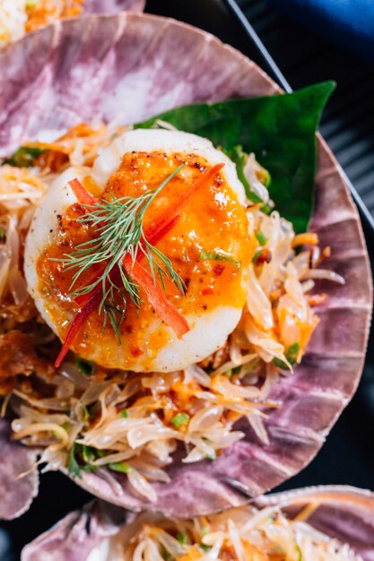 Bouchent Coquilles Saint-Jacques grillées en coquille avec salade de pomelo épicée servies dans une assiette noire.