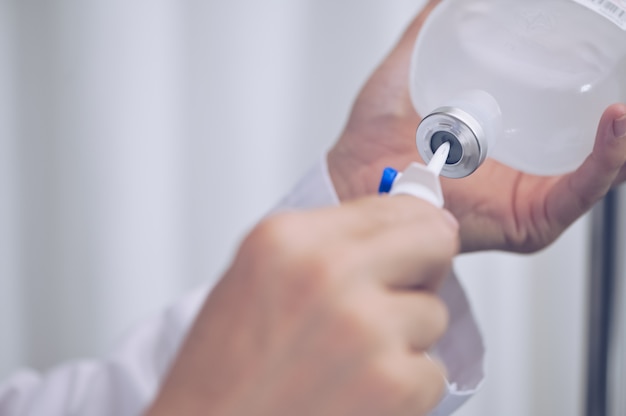 Bouchent le flacon d'injection de main de médecin pour perfusion perfusion intraveineuse saline avec solution IV pour patient à l'hôpital de salle