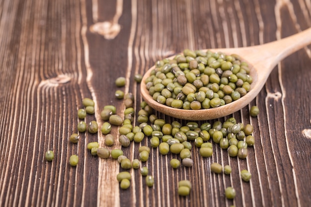 Bouchent les haricots mungo dans une cuillère en bois, mis sur fond de planche de bois