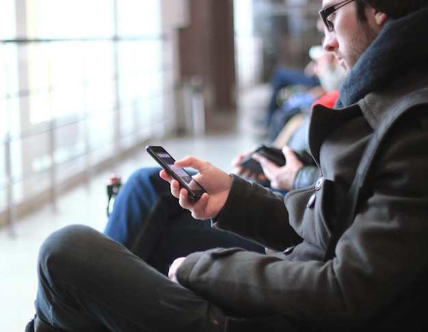 Bouchent l'homme moderne avec un smartphone assis dans le bâtiment de l'aéroport