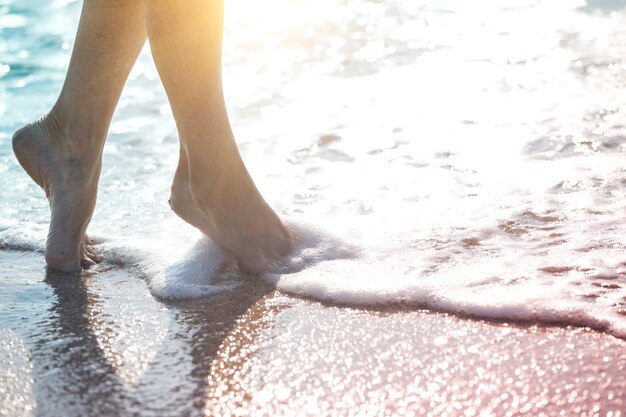 Bouchent la jambe de la jeune femme marchant le long de la vague d'eau de mer et de sable sur la plage d'été. Concept de voyage.