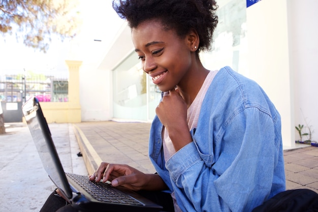 Bouchent les jeunes femmes américaines afro assis sur le trottoir et travaillant sur un ordinateur portable