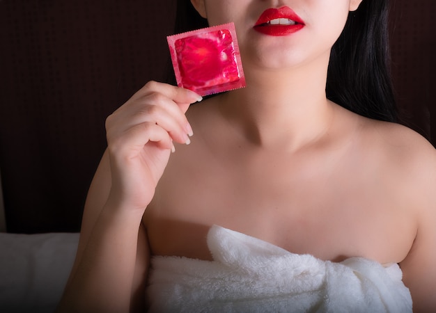 Bouchent les lèvres rouges femme main tenant le préservatif rouge sur fond noir
