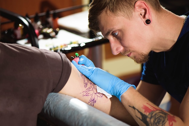 Bouchent la machine à tatouer. Homme créant une image sur place avec elle dans le salon.