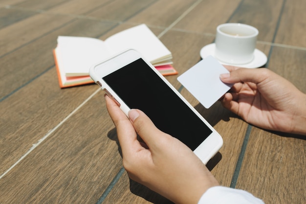 Bouchent la main de la femme tenant la carte de crédit et le téléphone mobile à écran blanc assis au café