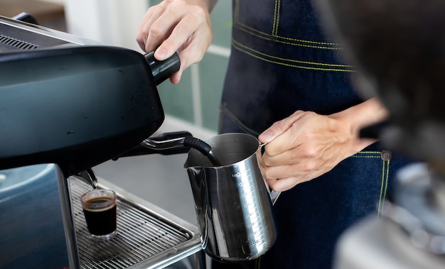 Bouchent la main tenant la crème fouettée avec du café. Faire une tasse de café dans une machine à café, la vapeur et la tasse. Machine à expresso avec porte-filtre en gros plan. Concept Cafetière au café.