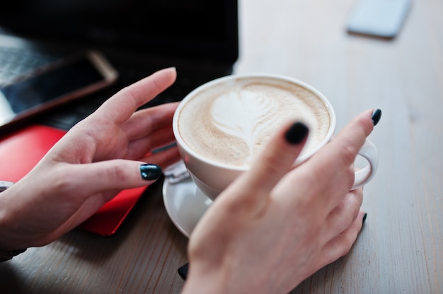 Bouchent les mains de la fille avec une tasse de cappuccino fond rouge pour ordinateur portable et téléphone portable.