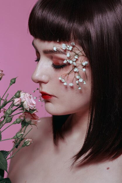 Bouchent le portrait de beauté de la belle jeune femme avec une peau fraîche, lisse et impeccable, maquillage nude avec fleur sur mur rose. Photo de mode