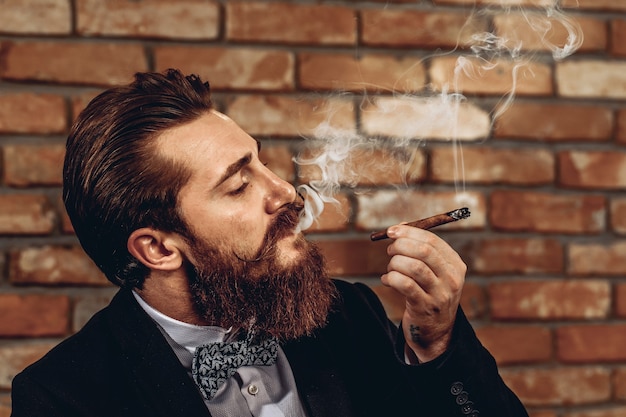 Bouchent le portrait d'un bel homme charmant avec une moustache et une barbe fumant un cigare brun