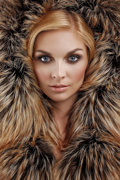 Bouchent le portrait de la belle fille en capuche de fourrure moelleuse sur la tête avec un maquillage parfait, des lèvres mates rouges et des yeux bleus.