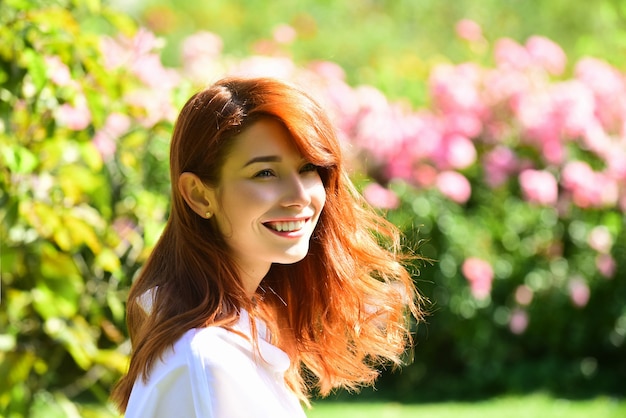 Bouchent le portrait d'une belle fille rousse debout sur une femme de fond de fleur dans le jardin