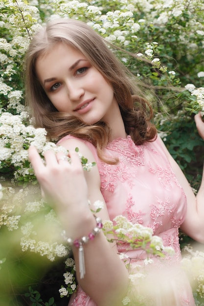 Bouchent le portrait d'une belle fille vêtue d'une robe vintage rose, debout près de fleurs colorées. Oeuvre d'art de femme romantique. Modèle de jolie tendresse regardant la caméra.