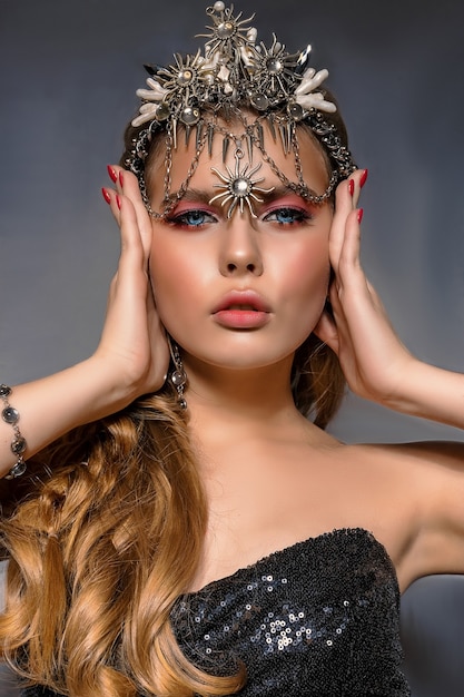 Photo bouchent le portrait d'une belle jeune femme blonde portant une couronne et des bijoux fantaisie sur fond gris.