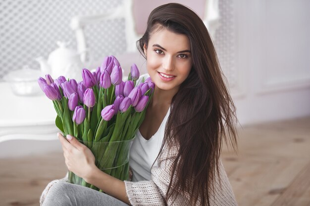 Bouchent le portrait de la belle jeune femme tenant des fleurs. Jolie femme aux tulipes