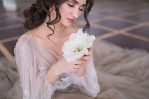 Bouchent le portrait de la belle mariée heureuse en robe de mariée avec une fleur assise sur le sol