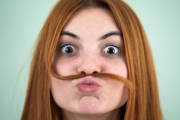 Photo bouchent le portrait de drôle de fille tenant de longs cheveux roux comme une moustache sous son nez.