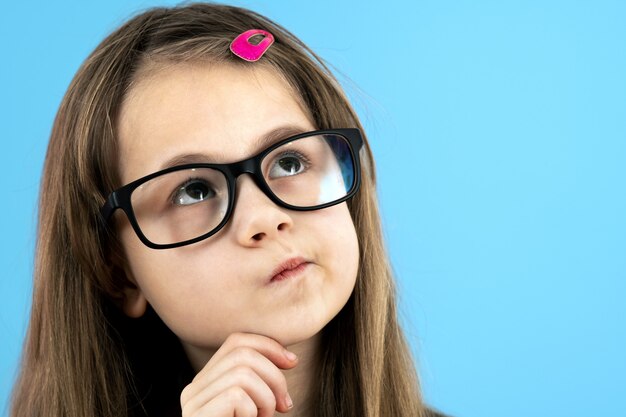 Bouchent le portrait d'une écolière enfant portant des lunettes tenant la main à son visage en pensant à quelque chose d'isolé sur fond bleu.