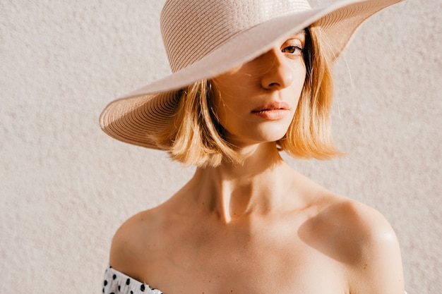 Bouchent le portrait d'élégante élégante fille blonde cheveux courts en chapeau posant sur fond blanc