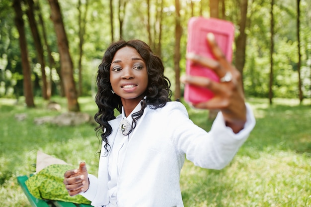 Bouchent le portrait de l'élégante fille afro-américaine noire prenant selfie avec téléphone mobile rose