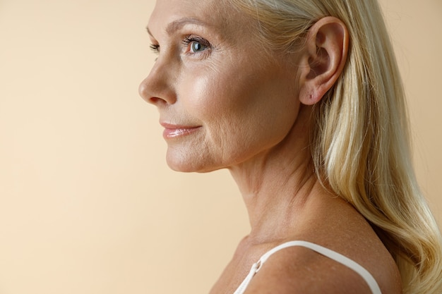 Bouchent le portrait d'une femme blonde mature en sous-vêtements blancs à l'écart posant isolé sur beige