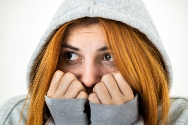 Bouchent le portrait d'une femme jeune rousse effrayée portant un pull à capuche chaud.