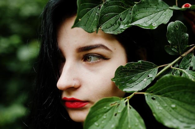 Bouchent le portrait d'une fille brune sensuelle avec des lèvres rouges. Goth femme dramatique à une branche d'arbre.