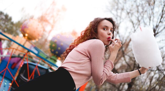 Bouchent le portrait d'une fille heureuse souriante et excitée tenant une barbe à papa au parc d'attractions