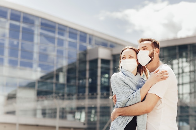 Bouchent portrait d'heureux homme et femme dans des masques de protection après la quarantaine des coronavirus. Jeune couple près de l'aéroport, ouverture des voyages en avion, concept de voyage