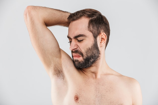 Bouchent le portrait d'un homme barbu dégoûté debout isolé sur blanc, sentant son aisselle