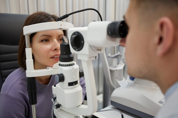 Bouchent le portrait de jeune femme à l'aide de machines pendant le test de vision dans une clinique d'ophtalmologie moderne