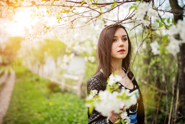 Bouchent le portrait de jeune femme brune avec des fleurs de cerisier au jardin de printemps.